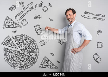 Smiling cook adding spices while cooking pizza Stock Photo