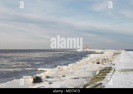 A sea mole with red lighthouse on the end covered in ice and freezing up sea. Stock Photo