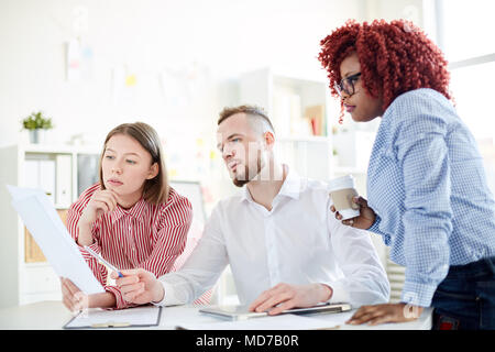 Multiethnic group of young concentrated male and female office workers reading important document together Stock Photo