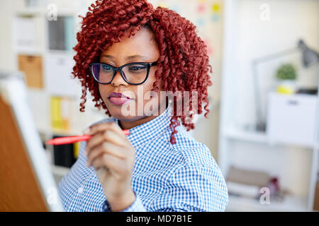 Red-haired African American female office worker writing plan of business meeting on whiteboard with marker Stock Photo