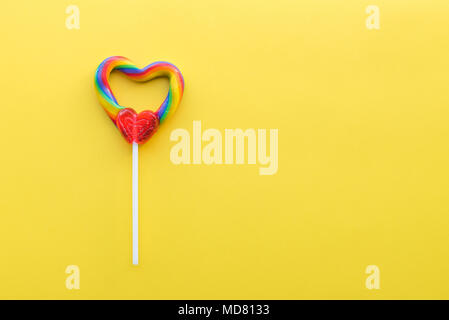 Heart shaped rainbow swirl lollipop on bright yellow solid background Stock Photo