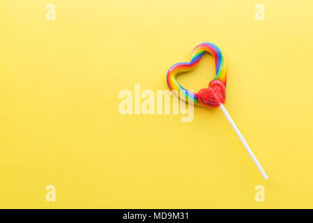 Single heart-shaped lollipop with rainbow swirl colors with bright yellow background Stock Photo