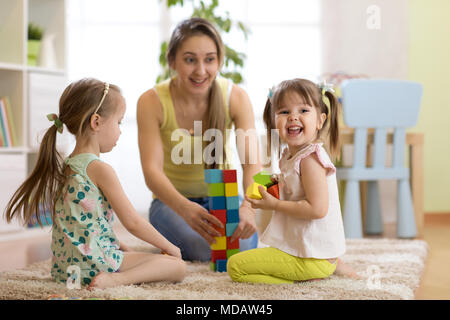 Happy family playing with cubes on the floor. Mother and children daughters spend fun time together. Stock Photo