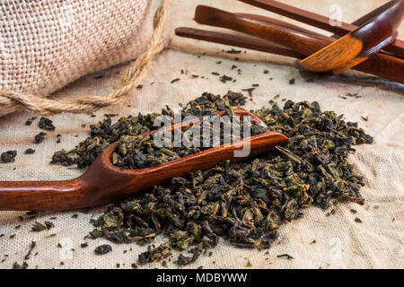 Chinese oolong  tea. Heap of tea leaves on textured linen tablecloth with bamboo spoon. Aromatic and healthy drink widely used in the world. Stock Photo