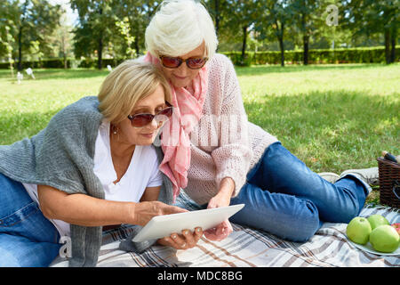 Two Senior Women Using Digital Tablet in Park Stock Photo