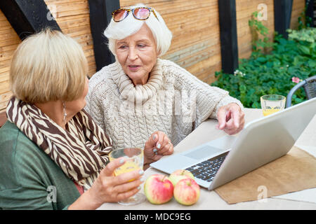 Two Senior Women Using Laptop Outdoors Stock Photo