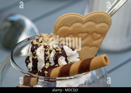 chocolate sauce on cream with hazelnut sprinkles and waffle in heart shape, close up Stock Photo