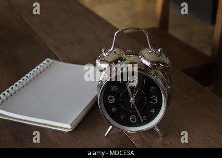 Retro alarm clock with blank realistic spiral notepad notebook on wooden table, stock photo Stock Photo