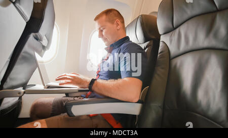 A young man was sitting on the plane and working on his laptop before departure. Stock Photo