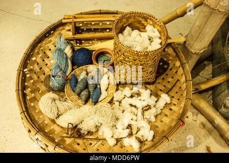 thai asian traditional cultural indigo color dyeing silk cloth process textile tools; yarn , shuttles, spun, etc. on brown rattan wooden sieve basket. Stock Photo