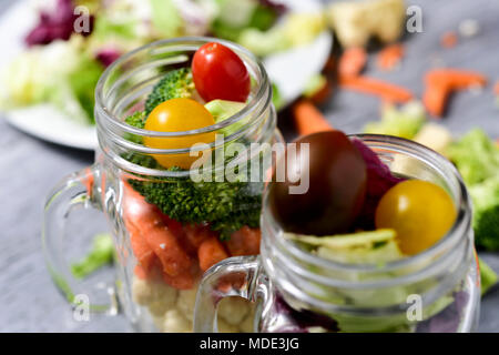 salad made with a mix of different lettuces, broccoli, green pepper, carrot and cherry tomatoes of different colors served in some mason jars, on a gr Stock Photo