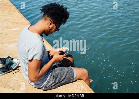 Man using mobile phone by edge of water Stock Photo