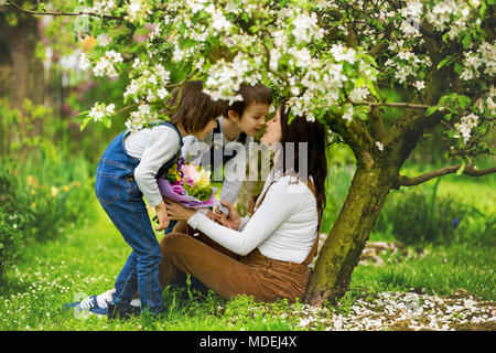 Young pregnant woman, receiving bouquet of colorful flowers from her children for Mothers Day, sitting in a beautiful spring blooming garden Stock Photo