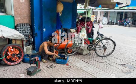 A Vietnamese bicycle repairman repairing a bike on the side walk in Ho Chi Minh City, Vietnam. Stock Photo