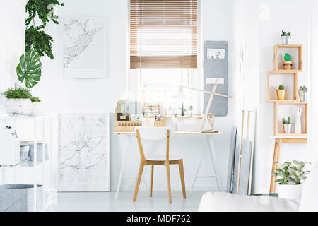 Bright home office interior with desk, wooden chair, shelf, plants and posters Stock Photo
