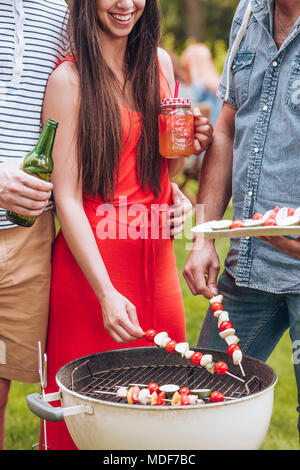 Group of friends grilling shashliks made of tomato and mozzarella in the garden Stock Photo