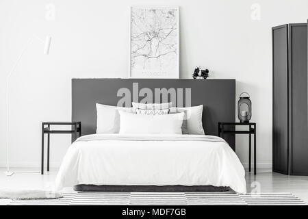 Poster on black bedhead in minimal hotel room interior with white bedsheets on bed Stock Photo