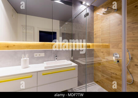 Mirrors above white cabinets with yellow handles in modern bathroom interior with glass shower door Stock Photo