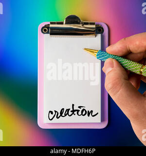 Writing pad with hand and pen poised to draw, write, sketch and be creative, isolated and presented on a colourful background, for creative design Stock Photo