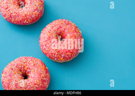 Pink frosted donut with colorful sprinkles on blue background. Top view. Copyspace Stock Photo