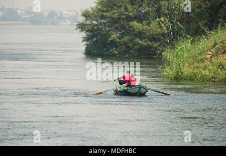 Traditional egyptian bedouin fisherman in rowing boat on river Nile fishing by riverbank Stock Photo