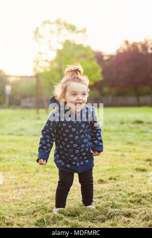 Little baby girl plays happy in the park outdoors in the spring against the backlight. Stock Photo