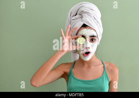 Teenage girl with a face mask on holding a cucumber slice in front of one eye Stock Photo