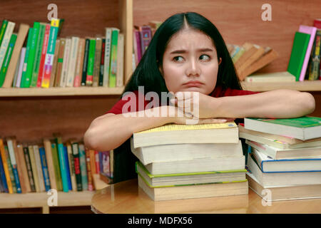 Asian student looking stressed while reading book preparing examination in library Stock Photo