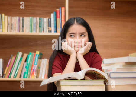Asian student looking stressed while reading book preparing examination in library Stock Photo