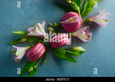 Pink macaroons decorated with pink and white alstroemeria flowers. Romantic French dessert on stone background with copy space. Stock Photo