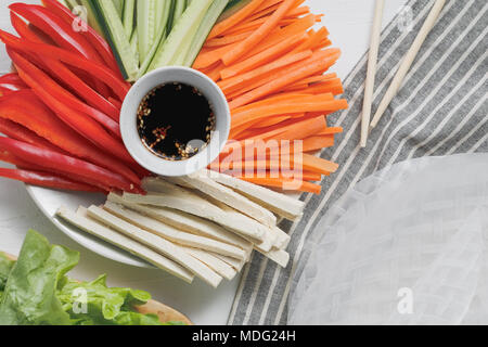 Ingredients for making asian fresh spring rolls. Raw cucumber, carrot, lettuce, bell pepper, tofu cheese inside rice paper. Top view. Stock Photo