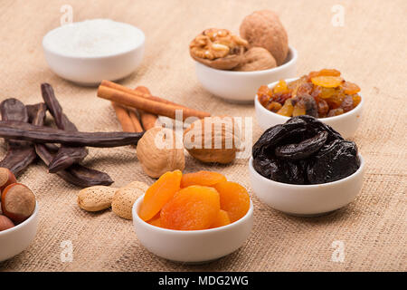 Mix of Ramadan Sweets - Dried fruits and nuts ( apricots, prunes, raisins, walnuts, hazelnuts, almonds, carob, and cinnamon) on sackcloth background Stock Photo
