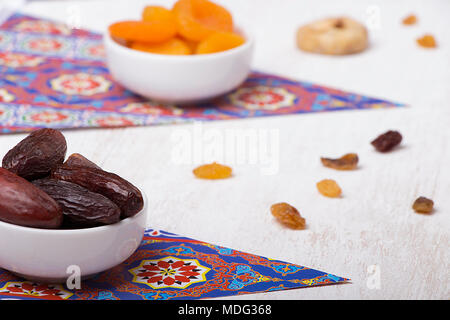 Ramadan Sweets - Dried Dates , Apricots , and Raisins above Islamic Shapes Fabrics on wooden table Stock Photo