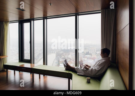 Attractive Man enjoying his morning coffee on his computer at his hotel room Stock Photo
