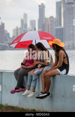 Three girls sitting on a wall watching something Stock Photo - Alamy