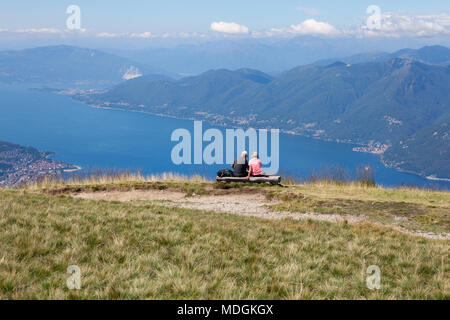 Two tourists contemplating the beautiful view of Lago Maggiore (Lake Maggiore) from the top of Monte Lema (Mount Lema). Veddasca, Italy Stock Photo