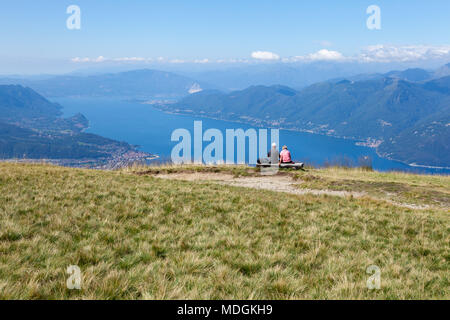 Two tourists contemplating the beautiful view of Lago Maggiore (Lake Maggiore) from the top of Monte Lema (Mount Lema). Veddasca, Italy Stock Photo