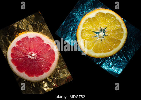 Sliced grapefruit and orange on a color foil on a black background Stock Photo