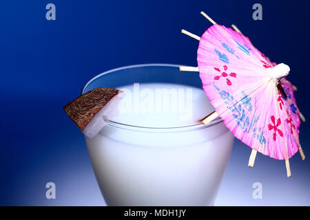 Glass of milk with a slice of coconut and a cocktail umbrella isolated on a blue background Stock Photo