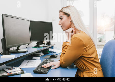 Image of young woman using computer while sitting at her desk in the office Stock Photo
