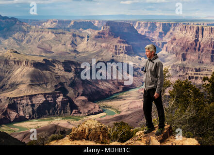 A senior man hiking in the Grand Canyon and standing on a ridge looking out over the landscape; Arizona, United States of America Stock Photo