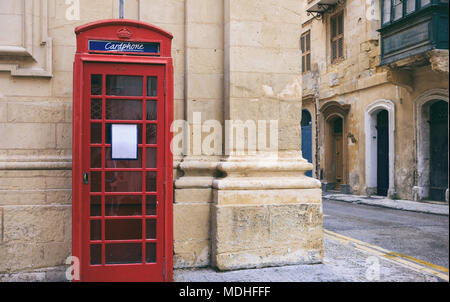 Red British vintage telephone booth outside of a sandstone facade building in Valletta, Malta Stock Photo