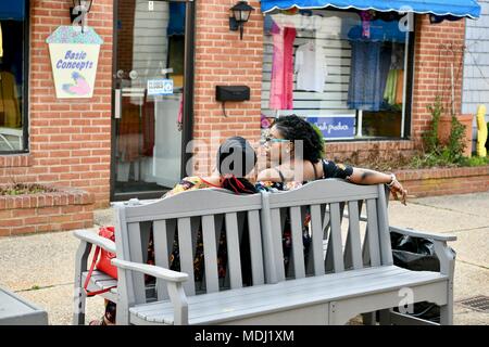 Two African American women sitting on a bench smoking cigarettes in public Stock Photo