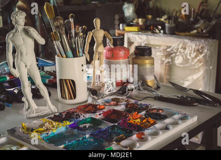 Acylic Color in Palette, Brush, Plaster Figure, Woodden Figure,  trowel on The Table in The Artist Sudio Stock Photo