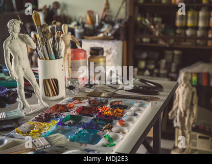Acylic Color in Palette, Brush, Plaster Figure, Woodden Figure,  trowel on The Table in The Artist Sudio Stock Photo