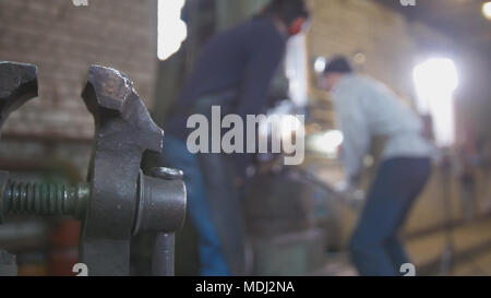 Blacksmith forging red hot iron on anvil - automatic hammering, de-focused Stock Photo
