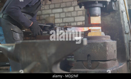 Blacksmith forging red hot iron on anvil - automatic hammering Stock Photo