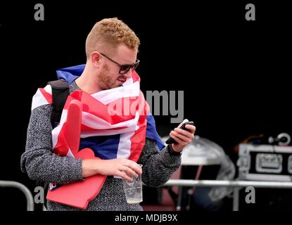 Man wearing sunglasses wrapped in Union Jack flag looking at mobile phone Stock Photo