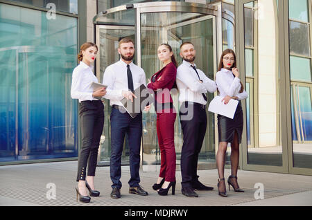 Command. Young office workers on the background of a multi-storey glass building. Five managers. Teamwork. Office. A group of people. Exchange Traders Stock Photo