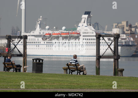 Gravesend, United Kingdom. 20th April, 2018. People relax at Gravesend Prom with cruise ship Astor pictured across the Thames at Tilbury. Gravesend in Kent is enjoying a baking hot day with high temperatures and bright sunshine. Gravesend often records the highest temperature of anywhere in the country. Rob Powell/Alamy Live News Stock Photo